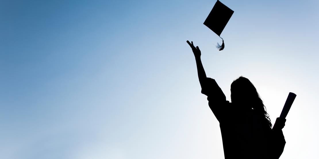 Silhouette of female graduate holding diploma in one hand and tossing grad cap into the air with the other hand