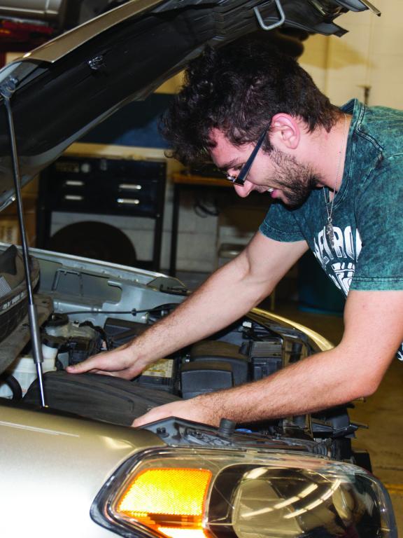 Automotive student works under hood of gold car