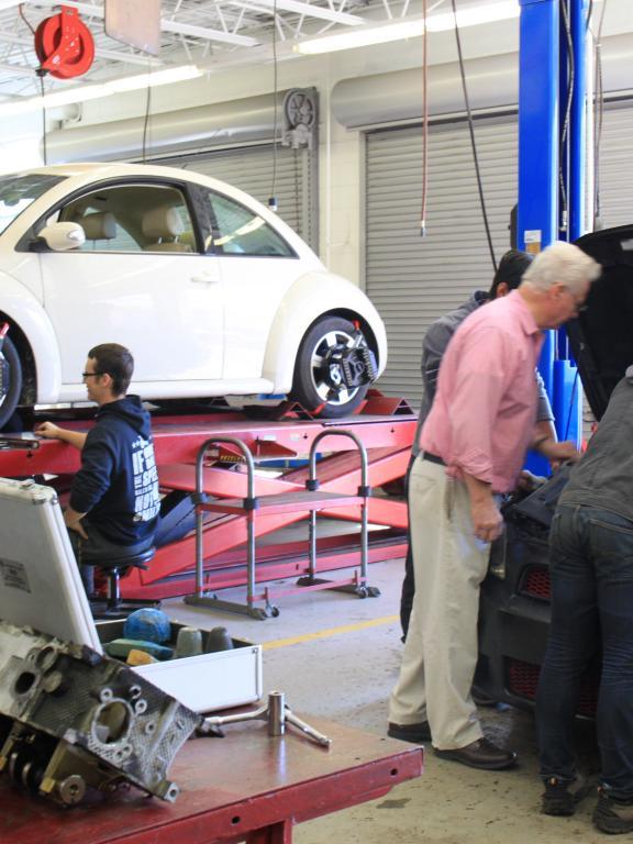 Automotive instructor looks on as students work on cars