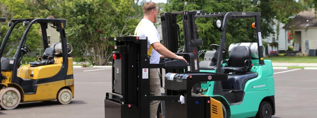 Instructor drives forklift next to two other forklifts in parking lot